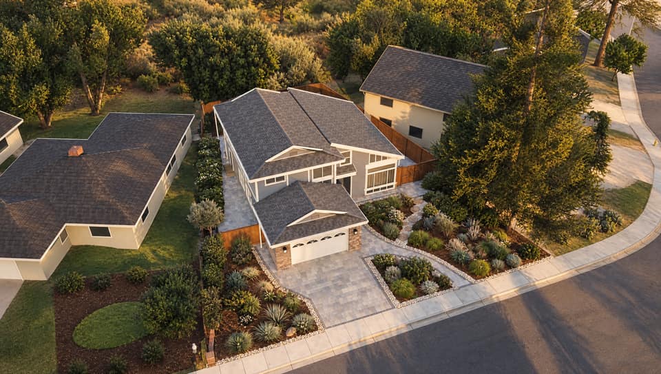 Concept render of the real project from above the street at golden hour: paver driveway and walk, bark beds edged in river rock, agaves and soft green mounds.